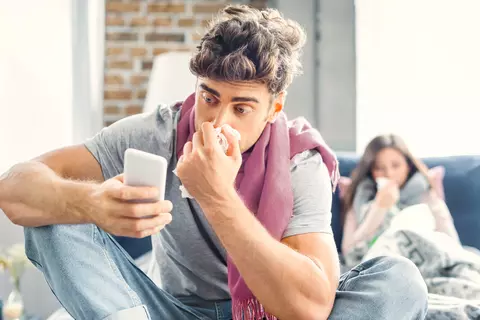 Un homme enrhumé navigue sur son téléphone portable