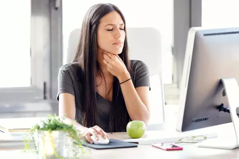 Frau mit Halsschmerzen vor dem PC